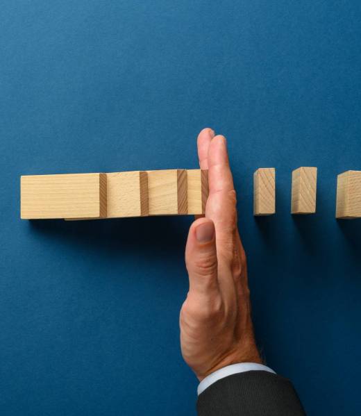 Top view of businessman hand interfering to stop collapsing dominos. Over blue background.